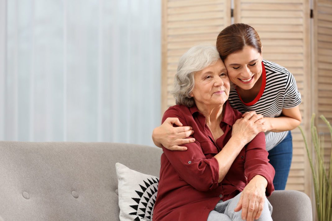 Elderly woman with female caregiver in living room. Space for te